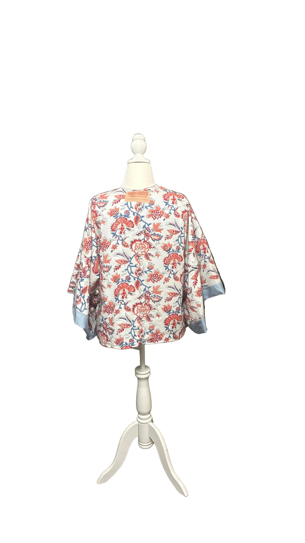 Floral jacket on a mannequin in a room with orange curtains and clothing racks.