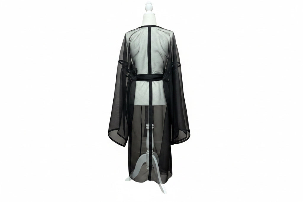 A black sheer mesh robe or kimono-style drape displayed on a white mannequin torso, shown from the back against a red curtain backdrop and wood floor.