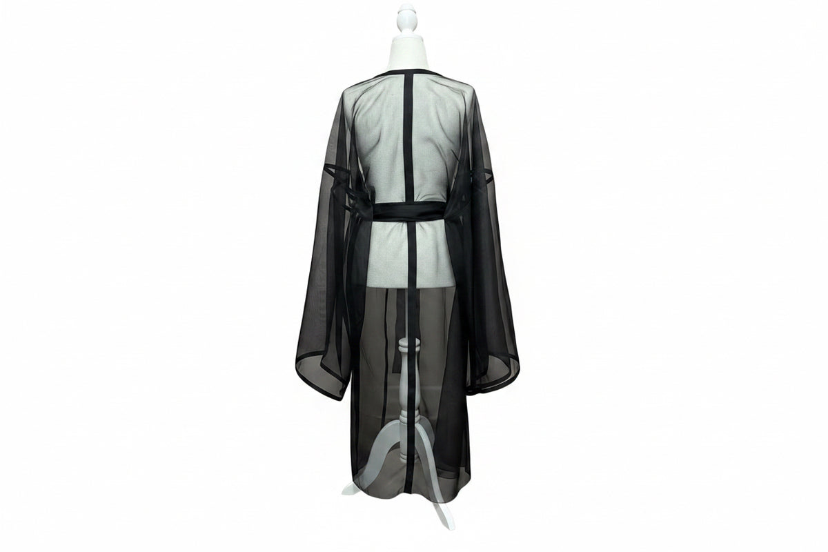 A black sheer mesh robe or kimono-style drape displayed on a white mannequin torso, shown from the back against a red curtain backdrop and wood floor.