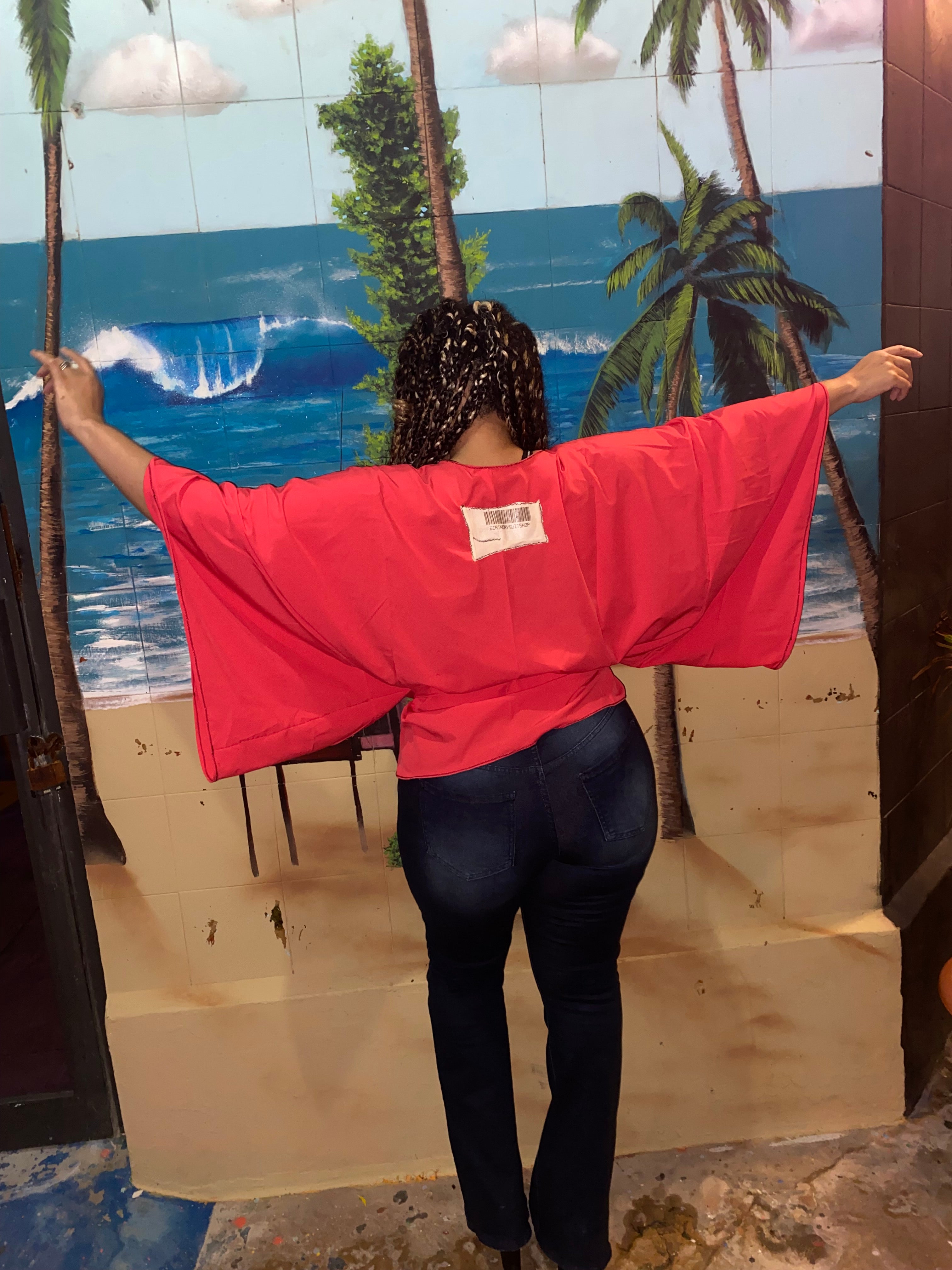 Person wearing a red jacket with a palm tree mural in the background
