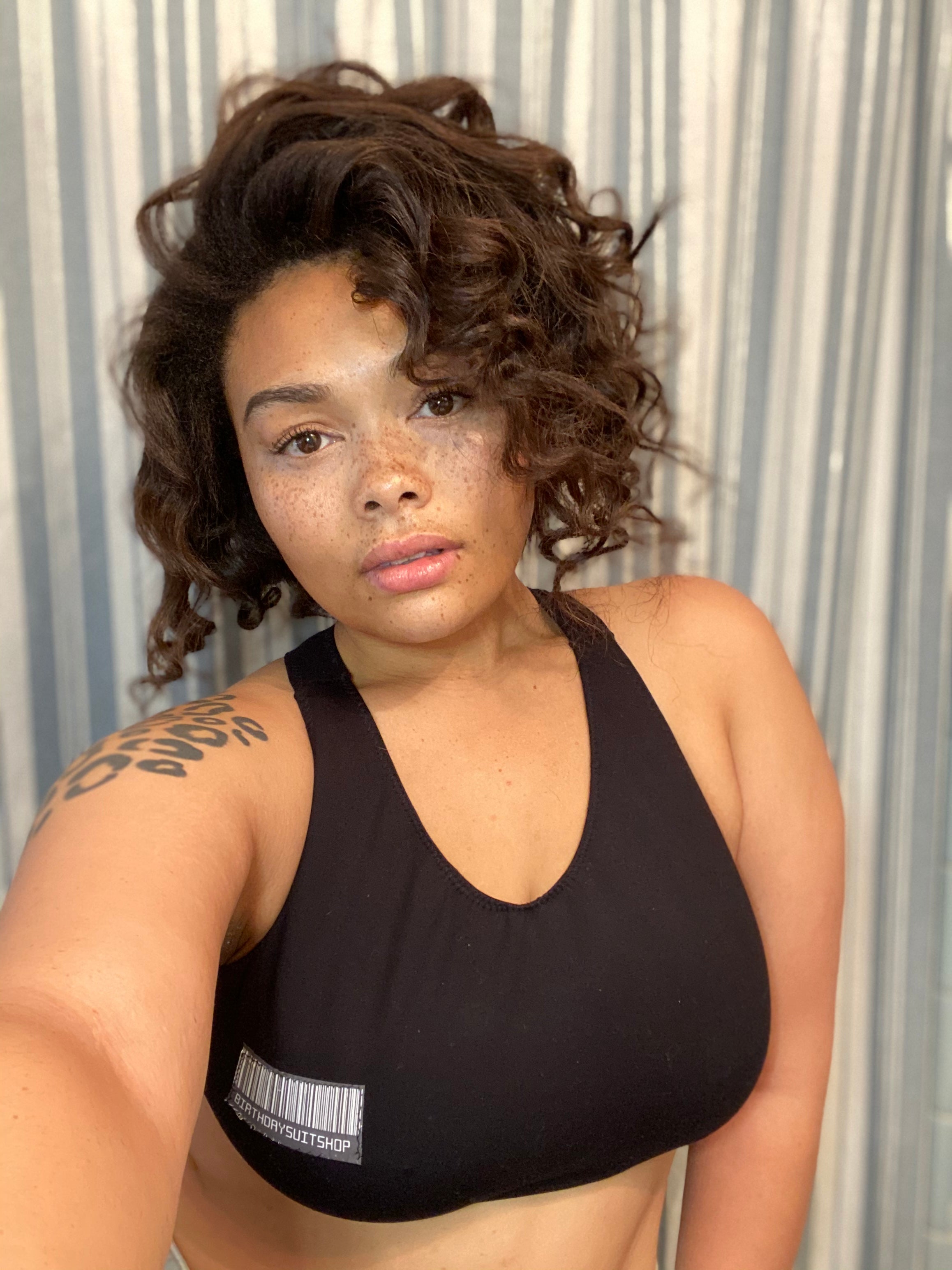 Person wearing a black sports bra with a visible brand logo against a striped curtain background