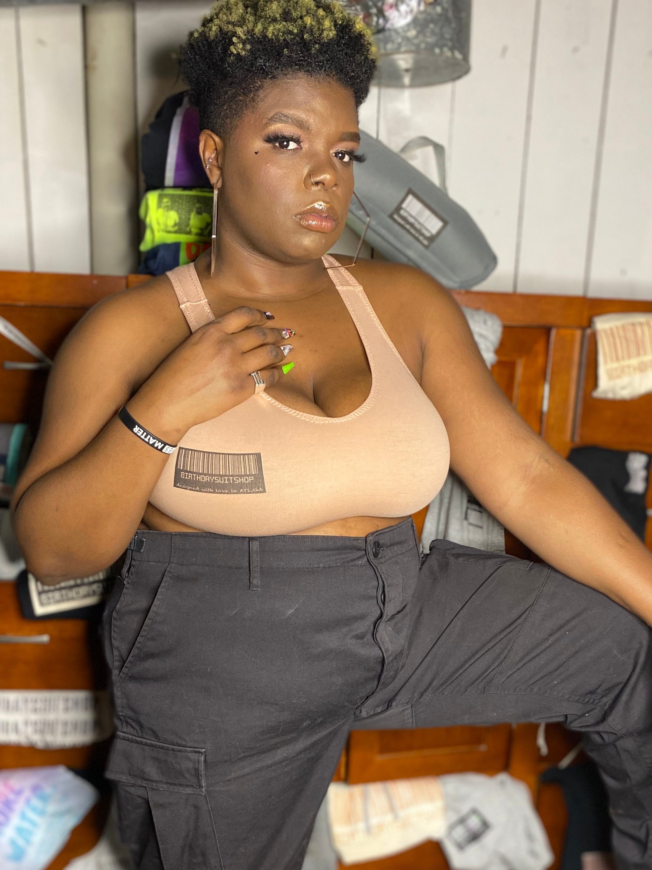 Person wearing a blush bralette and gray cargo pants in a room with wooden furniture and birthday suit shop clothes.